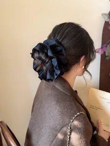 Detail of a large black satin scrunchie styling a low bun with a glossy silk texture