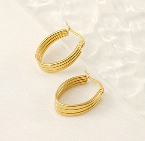 Vue détaillée de boucles d'oreilles créoles dorées en acier avec un design triple ligne