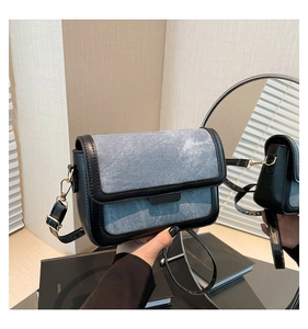 Detail of denim crossbody bag with gold metal buckle and leather trim on mirrors