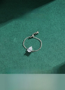 Detail of adjustable silver chain ring featuring a teardrop zircon on green texture