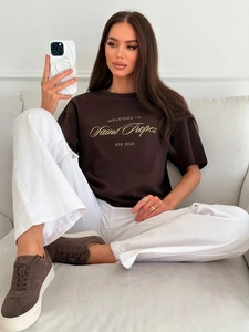Detail of loose dark brown cotton T-shirt featuring golden Saint Tropez art typography
