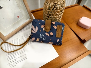 Detail of navy trifold wallet with autumn leaf print and brown leather brand tag
