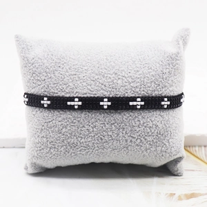 Minimalist black Miyuki beaded bracelet with white cross pattern on a plush jewelry pillow