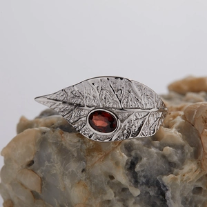 Detail shot of silver leaf ring featuring an oval red garnet set on a natural mineral base