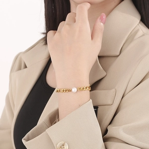 Detailed view of a gold chain pearl bracelet on a wrist with a beige blazer background