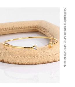 Detail view of gold-plated open bangle with cubic zirconia on a textured frame