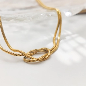 Detail view of gold snake bone chain necklace featuring a central decorative knot design