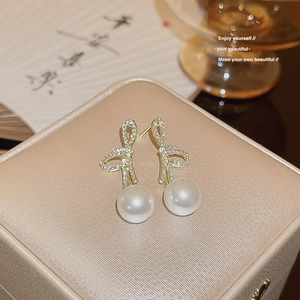 Elegant gold bow earrings with shimmering rhinestones and large white pearls on display