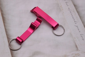 Close-up of pink metal keychain bottle openers on white fabric with wooden frame