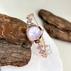 Macro detail of gold-tone watch band with pink gemstones and gradient dial face