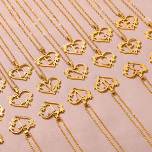 Collana a cuore dorato con lettere traforate e decoro floreale su tessuto rosa testurizzato