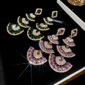 Macro shot of fan-shaped drop earrings with emerald and lilac zircon on black velvet
