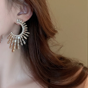 Close-up of sparkling gold C-shaped earrings with radiating rectangular zircons on model