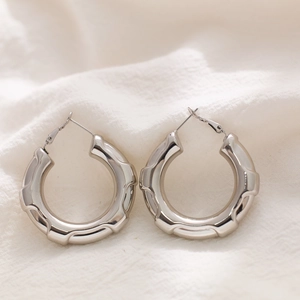 Polished silver titanium steel textured hoop earrings with bamboo wave design on white fabric