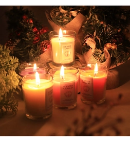 Primer plano de cinco velas aromáticas de colores en vasos con decoración festiva cálida