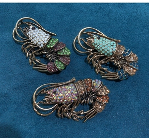 Detailed view of three vintage rhinestone lobster brooches on blue velvet background