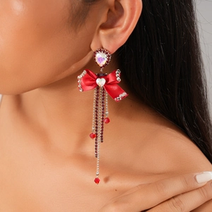 Close-up of long tassel earrings with red ribbon bow and shimmering iridescent gems