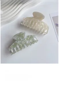 Close-up of pearl white and green marbled acetate hair claws on a decorative wave plate