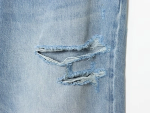 Dettaglio dei fori e dei bordi sfrangiati sul denim azzurro lavato a pietra