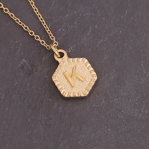 Macro shot of gold hexagon necklace with hammered texture and embossed letter K pendant