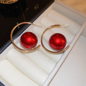 Macro shot of red pearl drop and gold hoop earrings resting in a white jewelry box