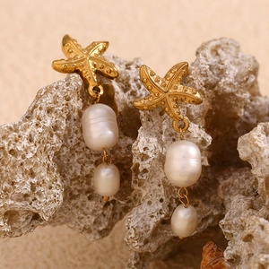 Detailed shot of 18K gold starfish earrings with white irregular pearls on coral