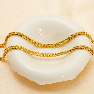 Macro shot of 40cm golden stainless steel cuban link chain necklace on white ceramic