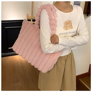 Detail of pink plush striped tote bag with decorative pom-pom handle on model