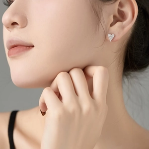 Macro close-up of a model wearing sparkling heart-shaped silver earrings with micro-pavé zircons