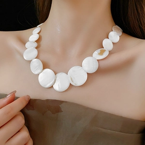 Close-up of geometric white shell necklace with gold bow detail on female model