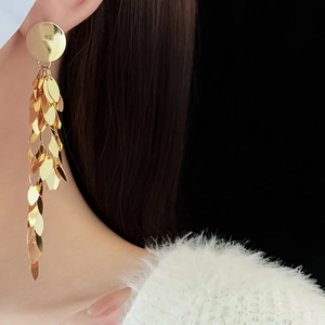 Detailed close-up of golden leaf sequin tassel earrings on model with metallic shine