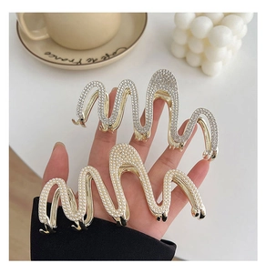 Close-up of gold pearl and silver rhinestone snake-shaped hair claws on a white surface