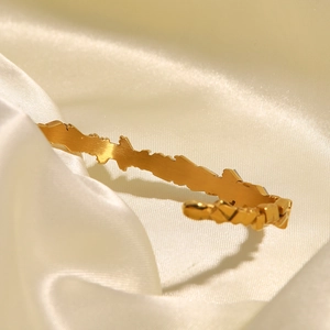Bracelet jonc doré en acier titane avec texture irrégulière sur soie beige élégante