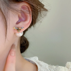Detail of bee stud earrings with sparkling crystals and large pearl backing on model