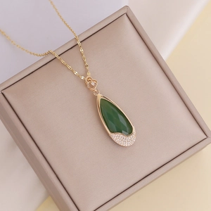 Close-up of golden waterdrop necklace with a green gem and pave set crystals