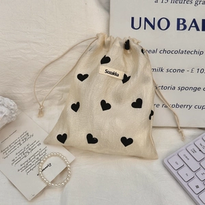 Detail of champagne drawstring pouch with black heart prints and woven logo label