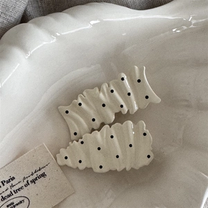 Close-up of cream resin hair clips with black polka dots on white shell tray