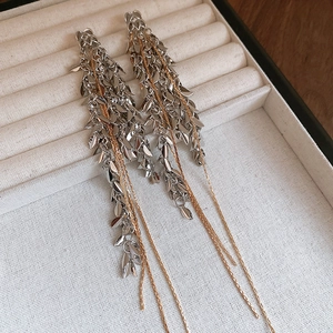 Détail de boucles d'oreilles à pompons avec feuilles argentées et chaînes dorées sur velours