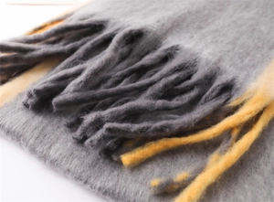 Close-up of soft grey and yellow tassels on a thick gradient knit winter scarf