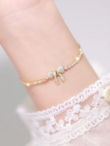 Detail of a gold bracelet featuring a bow charm paved with sparkling cubic zirconia stones
