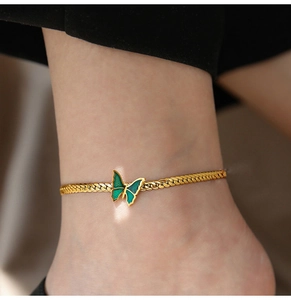 Detail of a gold woven anklet featuring a turquoise enamel butterfly charm on an ankle