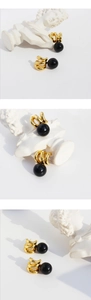 Macro detail of vintage gold wavy metal earrings with black onyx beads on white stone