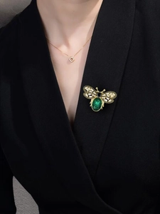 Detail of vintage gold bee brooch with green gemstone on black blazer lapel