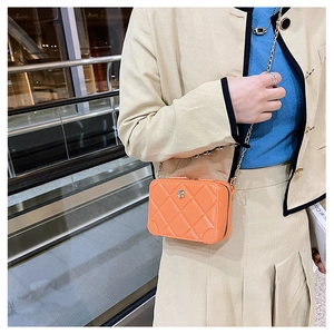Detail of orange PVC jelly bag with quilted texture and gold chain in suitcase style