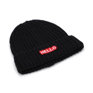Détail du bonnet en maille noire avec écusson HELLO rouge et texture côtelée