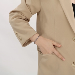 Detail eines silbernen Schweinenasen-Kettenarmbands getragen zum khakifarbenen Blazer