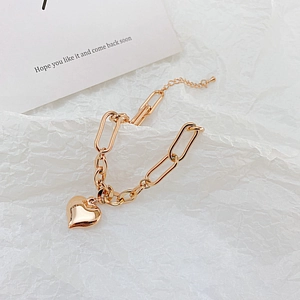 Macro shot of gold link bracelet featuring a polished heart charm on white textured paper
