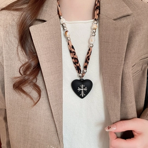 Detail of leopard print fabric necklace with heart pendant and silver cross charm