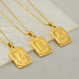 Detail of gold stainless steel rectangular pendants with embossed A, B, and C letters