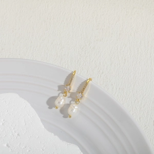 Detailed shot of gold freshwater pearl earrings with small zircon on ceramic tray